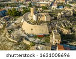 Aerial panoramic view of medieval Elda castle above the town with partially restored walls, towers and gate made of white lime stone in Spain