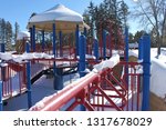Small photo of Playground covered in snow in winter, bright primary colors contrast with the floffy white snow and green conifers in the background. Pretence Park, Ashland, Wis.