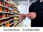 Small photo of A man standing in supermarket holding receipts compare the prices of grocery cost with previous months, upset by rising grocery prices and surging cost as an inflation financial crisis concept.