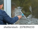 Small photo of Male person using squeegee cleaning glass windows with detergent foam at home.