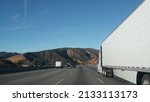 Lorry truck or semi-trailer on highway, freight cargo transportation in California USA. White container hauling or trucking on freeway road. Commercial transport logistics, van haulage. Cars driving.