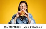 Girl bites cheeseburger with pleasure. Woman eating hambuger, order burger for takeaway food delivery at fastfood restaurant