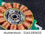 Small photo of Electric engine stator with coils copper wire winding or ball bearing on green PCB detail. Closeup of step motor inductors or metal ferromagnetic sheets from laser printer machine on blurry black net.