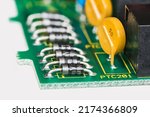 Small photo of Semiconductor diodes and yellow resettable fuses in PCB detail on white background. Closeup of electronic components as diode or round polymeric PTC device - polyswitch on green printed circuit board.