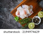 fish fillet on wooden board with ingredients for cooking, fresh raw pangasius fish fillet with herb and spices black pepper lemon lime and rosemary, meat dolly fish tilapia striped catfish - top view 