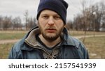 Small photo of Caucasian bum in dirty clothes with hat, cap. Sad beggar. Drunkenness, alcoholism. Below poverty line. refugee. Fugitive. Illegal immigrant. Medium Close Up shot