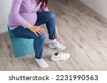 A pregnant girl with a big belly puts on sneakers on her feet. The concept of discomfort and inconvenience when bending over and putting on shoes. Convenient and comfortable shoes for pregnant women.