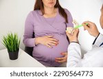 Small photo of doctor dentist holds a model of the dental jaw in his hands against the background of a pregnant woman. The concept of dental treatment during pregnancy.