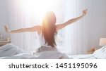 Small photo of Beautiful Brunette is Waking up in the Morning, Stretches in the Bed, Sun Shines on Her From the Big Window. Happy Young Girl Greets New Day with Warm Sunlight Flare.
