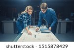 Small photo of In the Dark Industrial Design Engineering Facility Male and Female Engineers Talk and Work on a Blueprints Using Conference Table. On the Desktop Drawings, Drafts and Electric Engine Components, Parts