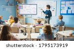 Elementary School Science Teacher Uses Interactive Digital Whiteboard to Show Classroom Full of Children how Software Programming works for Robotics. Science Class, Curious Kids Listening Attentively