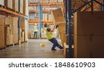 Small photo of Shot of a Warehouse Worker Has Work Related Accident. He is Falling Down BeforeTrying to Pick Up Heavy Cardboard Box from the Shelf. Hard Injury at Work.