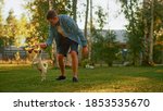 Small photo of Man Plays with His Smooth Fox Terrier Dog Outdoors. He Pets and Teases His Puppy with His Favourite Toy. Idyllic Summer House. Golden Hour Down Time.
