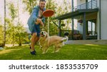 Small photo of Handsome Man Plays Catch flying disc with Happy Golden Retriever Dog on the Backyard Lawn. Man Has Fun with Loyal Pedigree Dog Outdoors in Summer House Backyard.