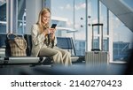 Small photo of Airport Terminal: Woman Waits for Flight, Uses Smartphone, Browse Internet, Social Media, Online Shopping. Traveling Female Remote Work Online on Mobile Phone in a Boarding Lounge of Airline Hub