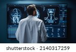 Small photo of Medical Hospital Research Lab: White Male Neuroscientist Looking at TV Screen, Analyzing Brain Scan MRI Images, Finding Treatment for Patient. Health Care Neurologist Curing People. Back View Zoom