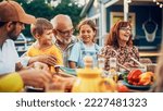 Small photo of Portrait of a Happy Senior Grandfather Holding His Bright Talented Little Grandchildren on Lap at a Outdoors Dinner Party with Food and Drinks. Family Having a Picnic Together with Children.