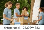 Small photo of Happy Team of Young Volunteers Preparing Humanitarian Aid Rations, Food, Donations and Loading Cardboard Boxes in a Van on a Sunny Day. Charity Workers Work in Humanitarian Donation Center.