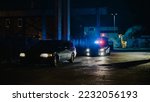 Small photo of Highway Traffic Patrol Car In Pursuit of Criminal Vehicle, Traffic Stop, Pull Over, Arrest. Police Officer Gets out of Squad Car, Approaches Suspect. Cinematic Action in Industrial Urban Area at Night