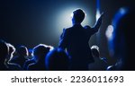 Small photo of Backview of a Stylish Young Businessman in a Dark Crowded Auditorium at a Startup Summit. Young Man Talking to a Microphone During a Q and A session. Entrepreneur Happy with Event Speaker.