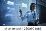 Small photo of Portrait of a Young Female Professor Explaining Big Data and Artificial Intelligence Research Project in a Dark Room with a Screen Showing a Neural Network Model. Computer Science Education in College