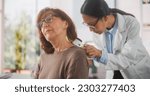 Small photo of Portrait of a Young Asian Dermatologist Using a Medical Magnifying Glass to Inspect any Damages on the Skin of a Senior Patient During a Health Check Visit to a Clinic. Doctor Working in Hospital