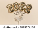 Small photo of beige festive background for the New Year or Christmas. Lying champagne glass from which golden stars have spilled out and gold foil balls in the shape of the number 2022