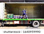 Small photo of Truck driver using ratchet tie down strapping to green and blue plastics box on the pallets in the truck.
