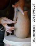 Small photo of Scrupulous work with raw clay: pottery production master adding details to potter vase or jug. Closeup of ceramist hands shaping ceramic tableware. Artistic occupation or small business manufacture