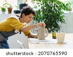 Small photo of Young female artisan concentrated on modeling jug from raw clay while pottery lesson or workshop in creative studio. Woman ceramic business owner making craft for sale in handmade potter retail store