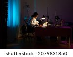 Small photo of Tailor studio interior with young designer creating clothes after work or studies. Creative female dressmaker working on sewing machine in workshop. Female seamstress small business owner at workplace
