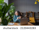 Happy female employee looking in window with satisfied face expression while sitting in office in front of laptop, woman taking break from computer work at workplace. Job satisfaction concept