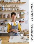 Small photo of Portrait of happy smiling self-employed pottery artist in creative studio working with raw clay shaping handmade cup or jar. Cheerful ceramics art teacher recording master class lesson in workshop