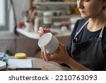 Small photo of Craftswoman creates new masterpiece in work studio making sketch of future pattern on white mug. Lady master wants to decorate kitchen with painted clay dish using pencil to draw interesting pattern