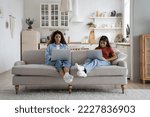 Modern introverted woman and teenage girl sits on sofa at home with laptops on laps. Unsociable Caucasian mother and child in casual clothes are addicted to gadgets and excessive use of internet