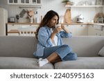 Small photo of Young woman sitting on sofa at home with cup tea and looking aside with smile on face, starting day with coffee. Calm contented female holding mug enjoying warm beverage, resting relaxing on weekend