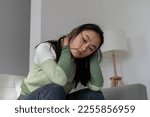 Small photo of Depressed despondent Asian girl suffering from stress after failure in personal relationship. Confused Japanese woman sits on sofa in living room clutching neck feeling sad due to professional burnout