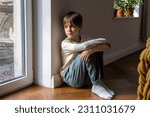 Small photo of Kid psychological trauma. Lonely child boy sadly look to window hug knees sits on floor at home alone. Upset offended child thinking about family problems, bad relationship, failures with school peers