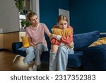 Small photo of Affectionate mom trying to establish contact with teenage daughter sitting on couch at home. Withdrawn girl turned away from mother, ignores attempts to help. Difficult teenager, problems at school.