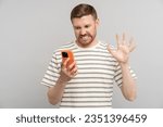 Small photo of Young man with disgust look at smartphone screen. Portrait of guy cringe and stare with aversion at phone display with squeamishness. Bad awful disgusting awkward joke or inappropriate content.