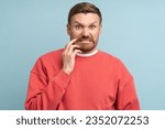 Small photo of Emotion of disgust on face of young man. Middle aged male in red sweatshirt on blue background with bright expressive facial expressions looks at camera contemptuously with hostility, loathing.