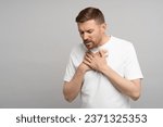 Small photo of Breathing problem. Man holds on to chest suffering from heartburn. Caucasian young guy suffers from pain in sternum. Unbearable pain tearing apart chest, burning inside and suffering, acute discomfort