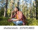 Small photo of Man hiker backpacker drinking tea eating snack sitting in forest has halt, resting. Tourist guy in summer warm day in woodland. Camping hiking tourism concept. Outdoors activity recreation on nature.