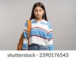 Small photo of Focused teen student girl with backpack on shoulder isolated studio background. Serious unsmiling joyless young teenager schoolgirl looking at camera. Beginning of academic year, admission to college