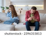 Small photo of Hopeless depressed woman desperately looking at window while man with indifferent face expression examines nails demonstratively ignoring wife. Toxic relations, disagreement, relationship problems