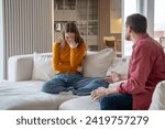 Small photo of Family conflict misunderstanding between spouses. Man screaming shouting gesturing hands. Toxic relationship, manipulation. Woman cry discussing with cruel man in abusive relations sits on couch.