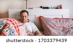 Man work and look at phone in bed. Work online from home. Quarantine, self isolation, depression, social distance, mental health concept. Stock photo.