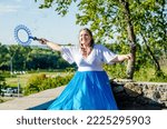 Street performer, beautiful young woman in blue skirt and white blouse, with soap bubbles shows soap show in summer in open air park for children