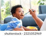 Small photo of Happy smiling boy with mom while eating in the living room at home. Preschool child development, food menu for 1 year olds