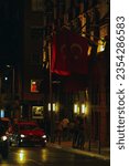 Small photo of Istanbul, Turkey - July 1, 2023; warm night cityscape, austere building with Turkish flags, road with red car and many pedestrians on sidewalk
